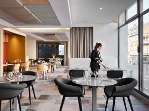 a woman walking through a restaurant with tables and chairs at Mercure Amiens Cathédrale in Amiens