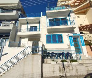 a white building with blue windows and chairs in front of it at Island House Kavala in Kavála
