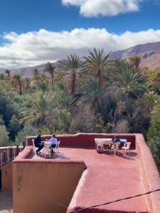 two people sitting at tables on a roof with palm trees at Auberge sahnoun in Tafraout