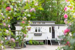 a white house with a porch and pink roses at Pipowagen de Luxe, prive hottub en zwembad in Heythuysen