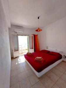 a bedroom with a red bed and a large window at Parostalkinghouse in Piso Livadi