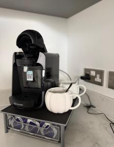a coffee maker and cups sitting on a shelf at Cosy flat that feels just like home in Leavesden Green