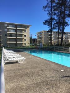 een zwembad met witte ligstoelen voor een gebouw bij Departamento Sol in El Tabo