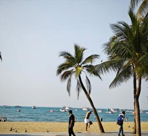 a group of people walking on a beach with palm trees at TM Room For Rent in Pattaya