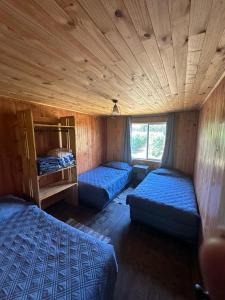ein Zimmer mit drei Betten in einem Holzzimmer in der Unterkunft Cabañas el rincón de Colbún in Colbún