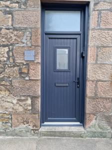 eine blaue Tür in einem Backsteingebäude mit einem Schild in der Unterkunft Rook View, Modern Coastal Retreat with Free Parking in Buckie