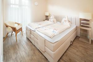 een witte slaapkamer met een bed met een stoel en een raam bij Utspann in Norderney +6 foto's