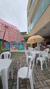 eine Gruppe von weißen Tischen und Stühlen mit Sonnenschirmen in der Unterkunft Aurora Peruíbe Hotel in Peruíbe