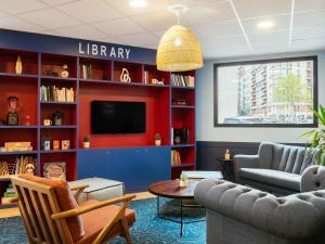 eine Bibliothek mit Fernseher, Sofa und Tisch in der Unterkunft Aparthotel Adagio Paris Malakoff Chatillon in Malakoff