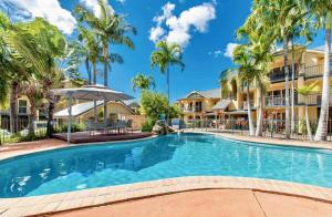 a swimming pool in front of a building with palm trees at Beach Road Bliss- Whitsundays in Cannonvale