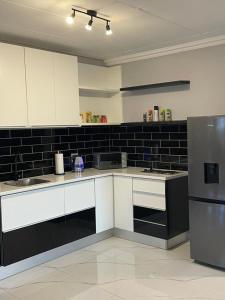 a kitchen with white cabinets and a black tile wall at Pine Self-Catering Unit in Windhoek +3 photos