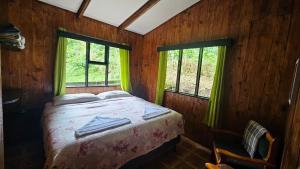 een bed in een houten kamer met 2 ramen bij Finca Terra Viva in Monteverde Costa Rica
