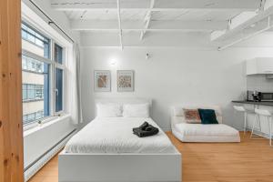 a white bedroom with a bed and a chair at Métropolitain Le Cachet in Quebec City