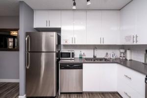 a kitchen with a stainless steel refrigerator and white cabinets at Stylish DT Condo ~2 Blocks from Stampede Grounds in Calgary