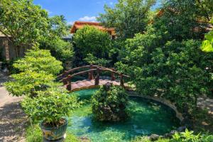 eine Brücke über einen Teich in einem Garten mit Bäumen in der Unterkunft ML Homestay in Bình Châu