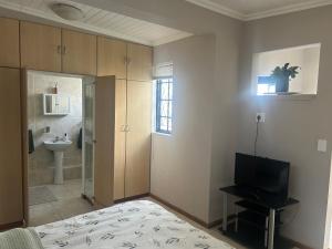 a bedroom with a bed and a television and a bathroom at The College Suite, Mill Park in Gqeberha