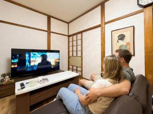 a man and woman sitting in a living room watching tv at Private House HidaTakayama - Cozy Family Home in Takayama