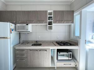 eine Küche mit Kühlschrank, Spüle und Mikrowelle in der Unterkunft Apartmento próximo ao mar in Capão da Canoa