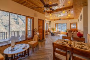 a dining room with tables and chairs and windows at SaffronStays Tirthan House - Balcony View in Bandal