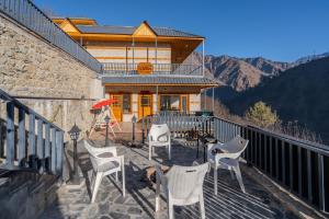 a balcony with chairs and a house with mountains at SaffronStays Tirthan House - Balcony View in Bandal