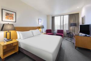 a hotel room with a large white bed and a television at Flagstaff Gardens Hotel Melbourne in Melbourne