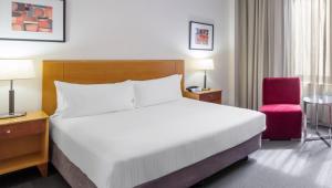 a bedroom with a large bed and a red chair at Flagstaff Gardens Hotel Melbourne in Melbourne
