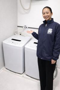 een vrouw staat naast twee wasmachines bij 宿屋しの軒 1階 in Kirishima