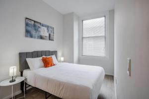 een witte slaapkamer met een groot bed met een oranje kussen bij CozySuites Sky Central #4 in Cincinnati
