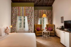 een slaapkamer met een bed en twee stoelen en een televisie bij Jetwing St Andrew's in Nuwara Eliya