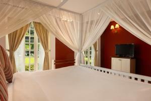 een slaapkamer met een wit bed met gordijnen en een televisie bij Jetwing St Andrew's in Nuwara Eliya +61 foto's