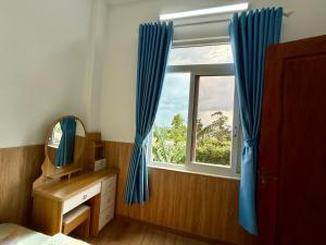 a bedroom with a window with blue curtains and a mirror at Villa 1985 in Buon Ma Thuot