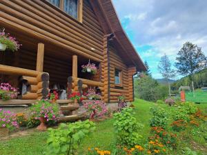 a log cabin with flowers in front of it at Stream House in Lopushnoye
