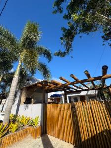 a wooden fence in front of a house with a palm tree at Residencial Rocha - Praia de Guaratiba - Prado - Ba in Prado