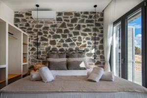 a bedroom with a stone wall and a bed with pillows at KYAN Syros in Liaropá