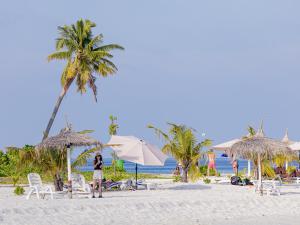 a woman standing on a beach with chairs and umbrellas at Kinan Retreat in Fulidhoo