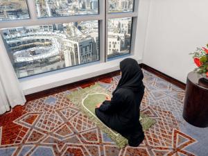 a woman sitting on a rug in a room looking out of a window at Swissotel Makkah in Makkah +231 photos