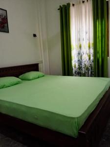 a bed with green sheets in a room with a window at Hurley vila in Weligama
