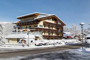 ein schneebedecktes Gebäude mit davor geparkten Autos in der Unterkunft Hotel Kasimir in Riezlern