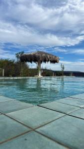 a pool with a straw umbrella next to the water at Villa carnaúbas in Pedro II