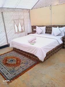a bedroom with a bed with white sheets and a rug at Raj Kesari Heritage Camp in Jaisalmer