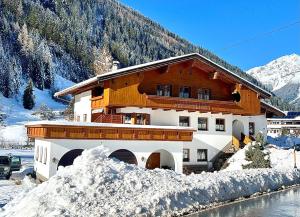 a building with snow on the ground next to a mountain at Apart Dorfbäck in Kaunertal
