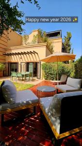 een patio met stoelen en tafels en een parasol bij Dar Hegoa Villa Soleil et Chaleureuse in Marrakesh