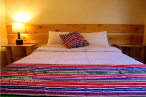 a bed with a colorful striped blanket and a lamp at Fundo Alma Andina in Jauja