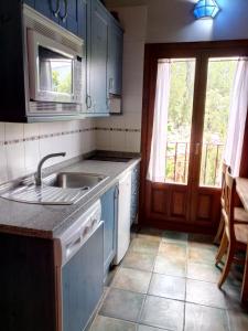 een keuken met blauwe kasten, een wastafel en een raam bij El Refugio de la Sauca in Alameda del Valle