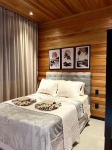 a bedroom with a bed with white sheets and pictures on the wall at Cabana Maciambu casa de praia Palhoça SC in Palhoça