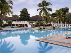 a swimming pool with palm trees and a building at Novotel Goa Dona Sylvia Resort in Cavelossim