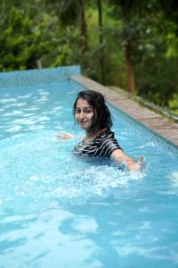 a woman is swimming in a swimming pool at Ayurnest Pool Resort Wayanad in Batheri