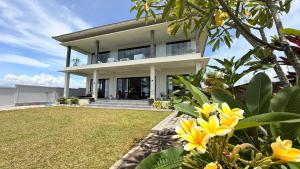 a large white house with yellow flowers in the yard at Ocean Daze Villa Yehsumbul in Jembrana
