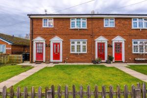 a brick house with red doors and a fence at 2 BDR House By Eason Stays Short Lets Stockport in Stockport