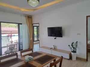 a living room with a table and a tv on a wall at Bancha white house in Ban Bo Han
